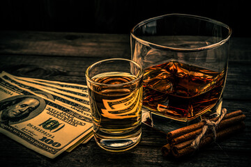 Glass of brandy and tequila with money and cinnamon sticks tied with jute rope on an old wooden table. Angle view