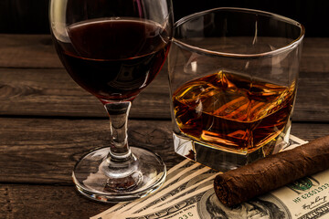 Glass of brandy and red wine with money and cuban cigar on an old wooden table. Angle view