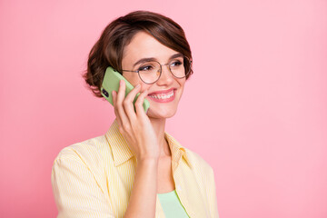 Photo of pretty cute young woman wear yellow shirt glasses talking modern device looking empty space isolated pink color background