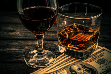 Glass of brandy and red wine with money on an old wooden table. Angle view