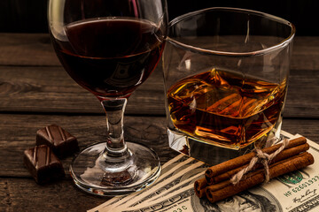 Glass of brandy and red wine with money and  chocolate with cinnamon sticks tied with jute rope on an old wooden table. Angle view