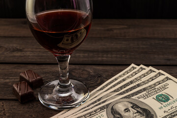Glass of red wine and chocolate with money on an old wooden table. Angle view