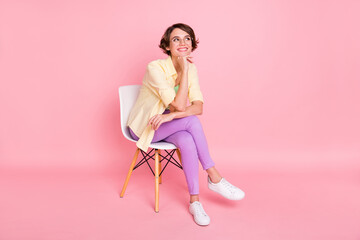 Photo of sweet dreamy young woman wear yellow shirt arm glasses sitting chair looking empty space isolated pink color background