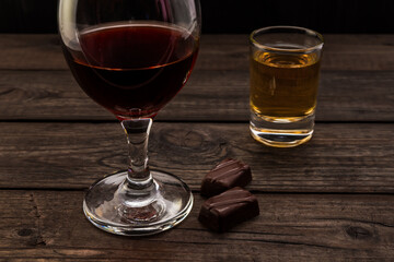 Glass of red wine and tequila with chocolate on an old wooden table. Close up view