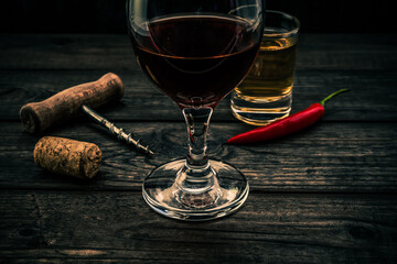 Glass of red wine and tequila with corkscrew and cayenne pepper on an old wooden table. Close up view, focus on the glass of red wine