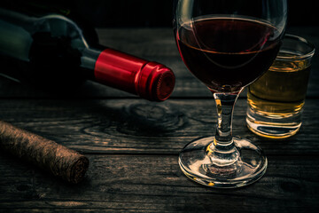 Glass and bottle of red wine with tequila and cuban cigar on an old wooden table. Close up view