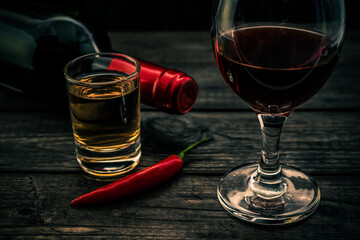 Glass and bottle of red wine and tequila with cayenne pepper on an old wooden table. Close up view, focus on the glass of red wine