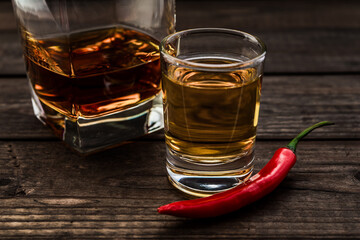 Glass of brandy and tequila with cayenne pepper on an old wooden table. Close up view