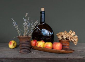 Still life with ripe apples, a large brown glass bottle and a bouquet of lavender in a ceramic vase. Vintage.