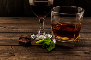 Glass of brandy and red wine with mint sprig and chocolate on an old wooden table. Close up view