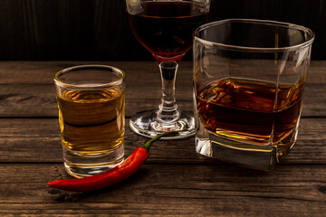 Three glasses with brandy, tequila and red wine with cayenne pepper on an old wooden table. Close...