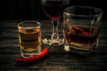 Three glasses with brandy, tequila and red wine with cayenne pepper on an old wooden table. Close up view