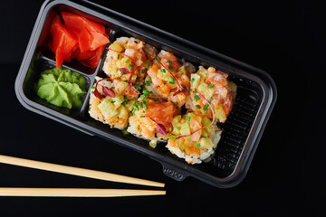 Fresh sushi rolls with shrimp, crab served in lunch box for takeaway. To go Japanese sushi food concept for healthy lunch. Closeup top view on black background.