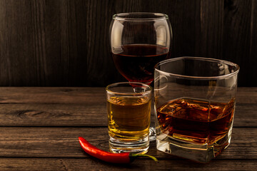 Three glasses with brandy, tequila and red wine with cayenne pepper on an old wooden table. Angle view