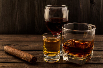 Three glasses with brandy, tequila and red wine with cuban cigar on an old wooden table. Angle view