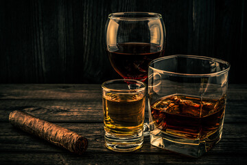 Three glasses with brandy, tequila and red wine with cuban cigar on an old wooden table. Angle view