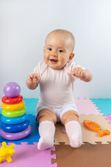 Fototapeta na wymiar Joyful baby with toys. Laughing Newborn on a Colorful Puzzle Mat