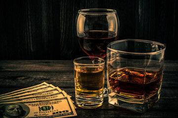 Three glasses with brandy, tequila and red wine with money on an old wooden table. Angle view