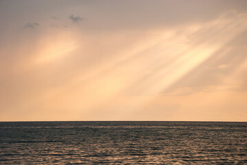 The rays of the sun break through the clouds onto the water smooth of the sea.