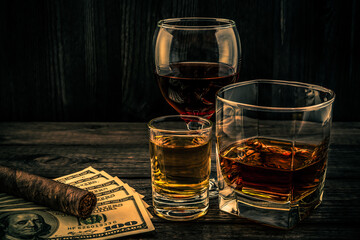 Three glasses with brandy, tequila and red wine with money and cuban cigar on an old wooden table. Angle view