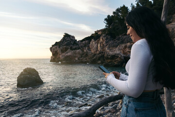 woman using mobile in front of a sunset in the sea