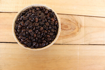 Coffee beans in the wicker basket isolated on wooden background closeup.