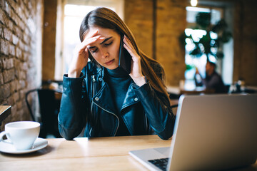 Puzzled skilled woman with netbook feeling stressful during consultancy conversation for discuss trouble of web programming, unhappy female freelancer with laptop using mobile application for call