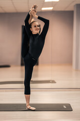 Fototapeta premium Beautiful young woman is engaged in gymnastics in the gym. The athletic body of the girl is covered with tight-fitting yoga clothes.