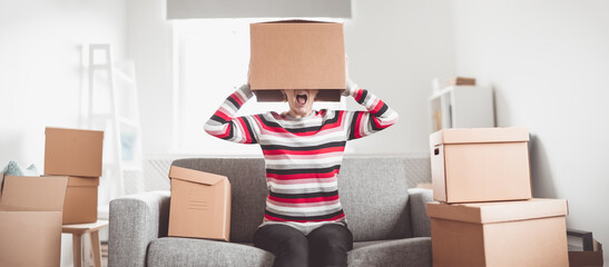 Tired woman with cardboard box on her head sitting on the sofa in her new house.