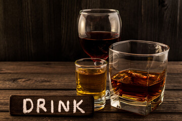 Three glasses with brandy, tequila and red wine with the wooden plank on it is an inscription 