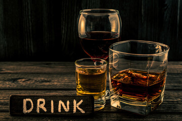 Three glasses with brandy, tequila and red wine with the wooden plank on it is an inscription 