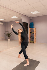 Beautiful young woman is engaged in gymnastics in the gym. The athletic body of the girl is covered with tight-fitting yoga clothes.