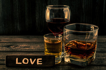 Three glasses with brandy, tequila and red wine with the wooden plank on it is an inscription 