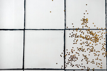 Spilled golden glitter sequins on white tile floor or countertop background. Copy space. Top view.
