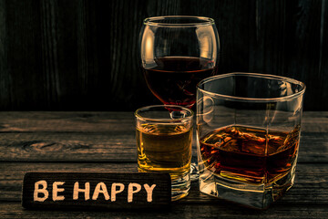 Three glasses with brandy, tequila and red wine with the wooden plank on it is an inscription 
