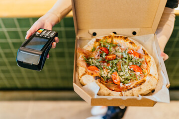 Service payment for services, unrecognizable waiter holding pizza in open box waiting for payment for the order without contact payment.