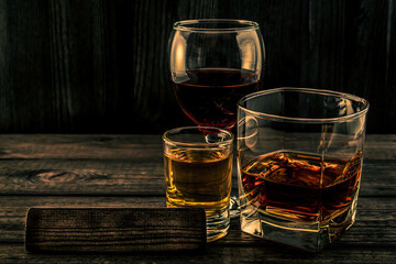 Three glasses with brandy, tequila and red wine with the empty wooden plank on an old wooden table. Angle view focus on the wooden plank