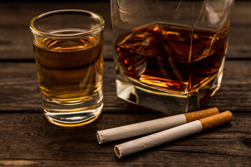 Glass of brandy and tequila with cigarettes on an old wooden table. Close up view, focus on the...