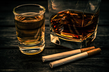 Glass of brandy and tequila with cigarettes on an old wooden table. Close up view, focus on the...