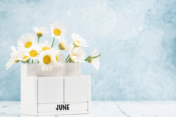 cube calendar for June with daisy flowers over blue background