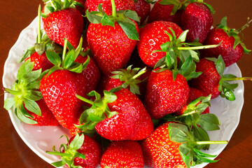 Ripe red strawberries in a white plate on a wooden table, summer, July