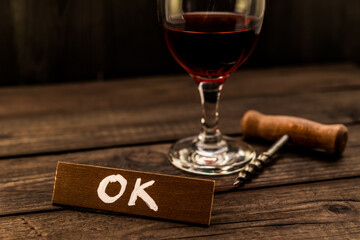 Glass of red wine with corkscrew and the wooden plank on it is an inscription 