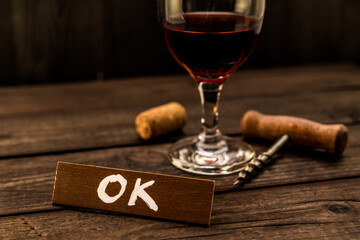 Glass of red wine with corkscrew and cork with the wooden plank on it is an inscription 