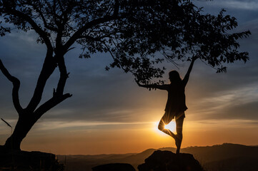 Silhouette of a  young woman practicing yoga on the mountains with a beautiful sunset