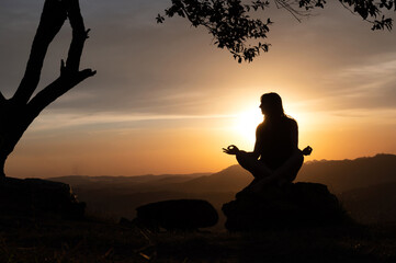 Silhouette of a  young woman practicing yoga alone on the mountains with a beautiful sunset