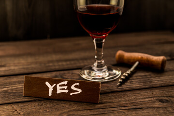 Glass of red wine with corkscrew and the wooden plank on it is an inscription 