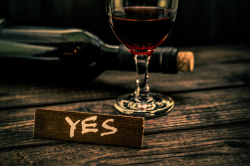 Glass and bottle of red vine with the wooden plank on it is an inscription 