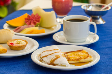 Brazilian tapioca with rennet cheese baked on a breakfast table. Cup of coffee, with cut fruits, muffin, bread on a blue tablecloth. Northeastern Brazilian cuisine.