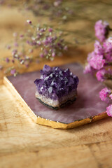 Rose quartz coaster with violet amethyst crystal and pink flowers. Mystical altar on wooden background. Gentle meditative and yoga concept. 