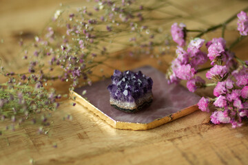 Rose quartz coaster with violet amethyst crystal and pink flowers. Mystical altar on wooden...